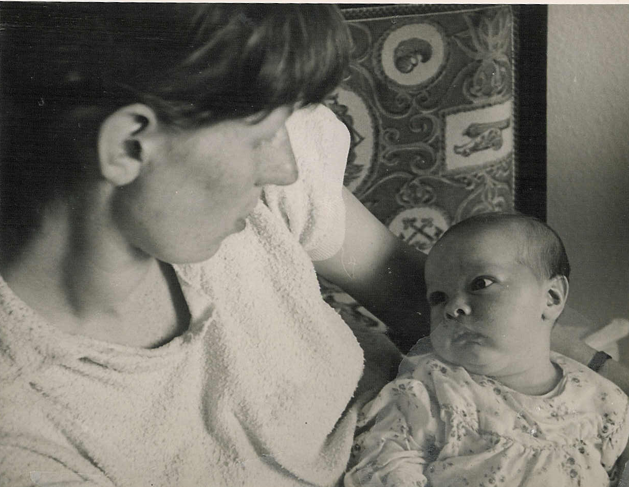 A historical black and white photograph of Sue holding baby Andy, looking towards each other.