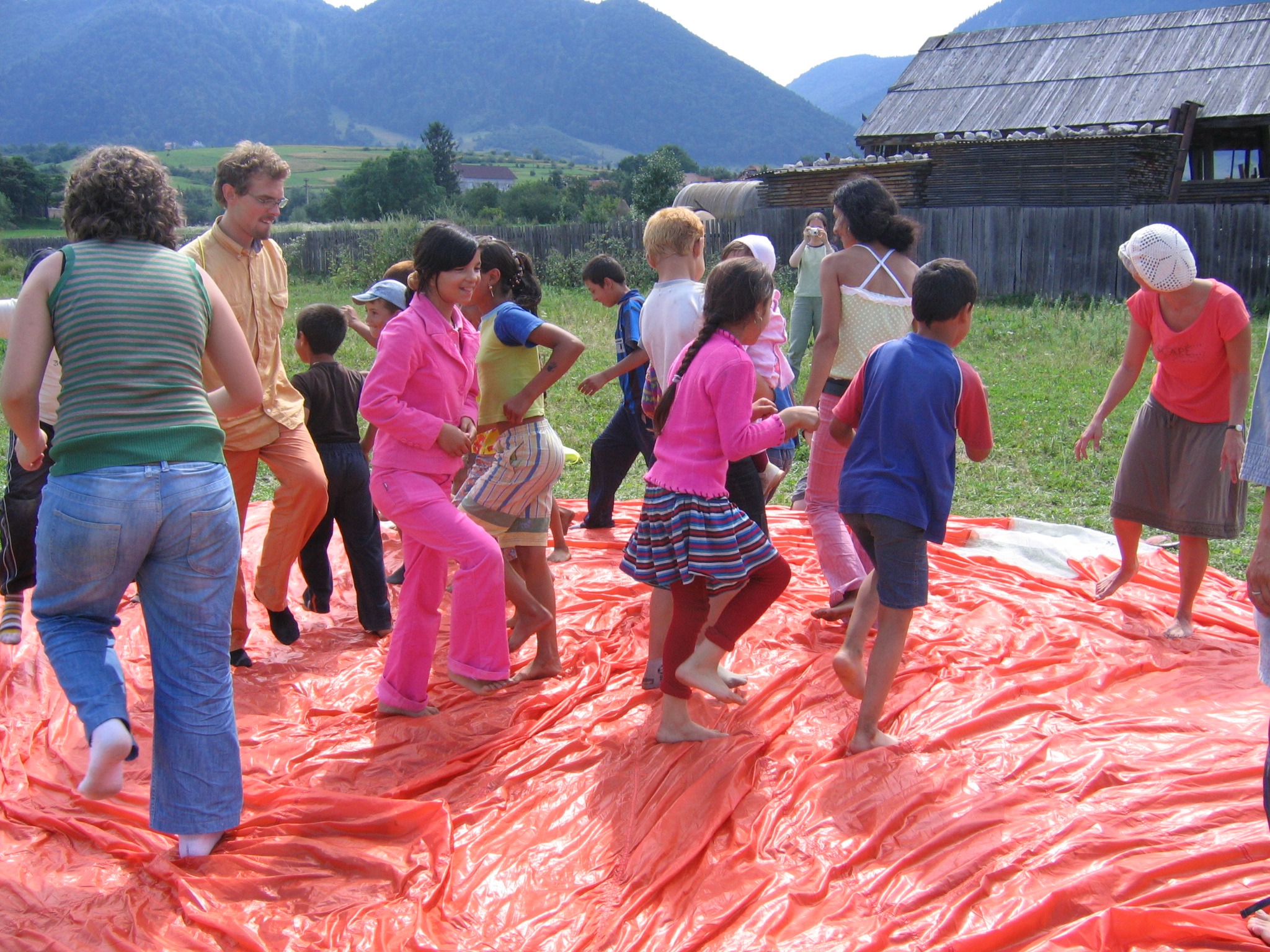 Children and adults moving on a large bright orange sheet outdoors