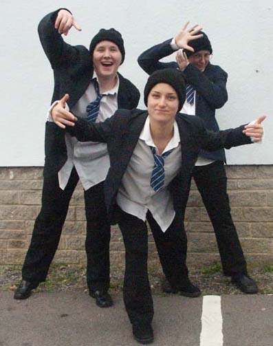 Three performers in matching costumes making gestures outdoors